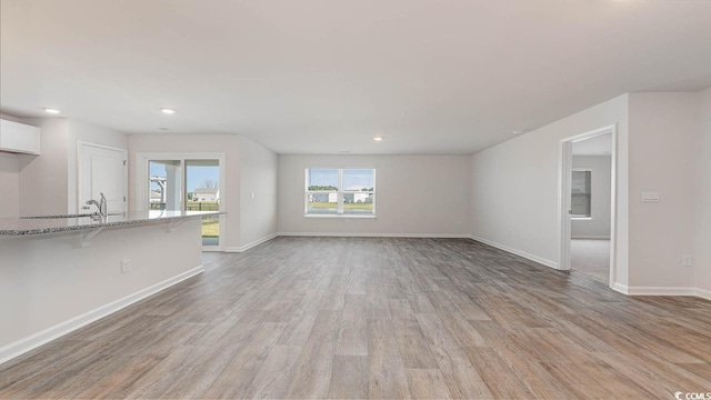 unfurnished living room with recessed lighting, baseboards, and light wood finished floors