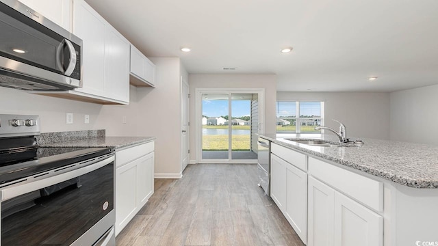 kitchen with light stone counters, appliances with stainless steel finishes, white cabinetry, a sink, and light wood-type flooring