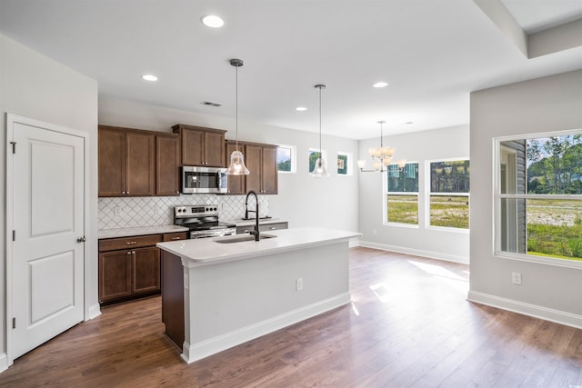 kitchen featuring a sink, stainless steel appliances, an inviting chandelier, a center island with sink, and backsplash