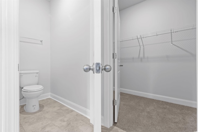 bathroom with baseboards, toilet, and a walk in closet