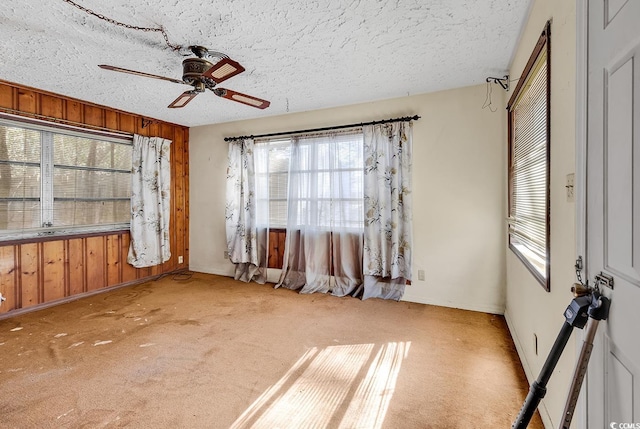 carpeted empty room with ceiling fan, a textured ceiling, and wood walls