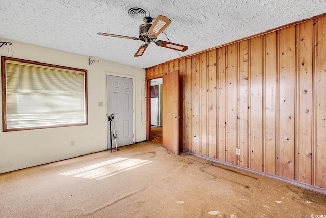 unfurnished room featuring ceiling fan, carpet flooring, a textured ceiling, and wood walls