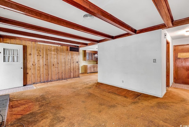 unfurnished living room featuring beam ceiling, wooden walls, and carpet flooring