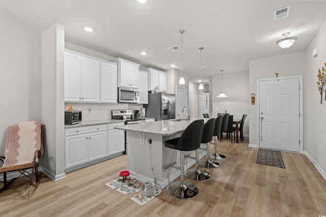 kitchen with a breakfast bar area, appliances with stainless steel finishes, light stone countertops, a kitchen island with sink, and white cabinets