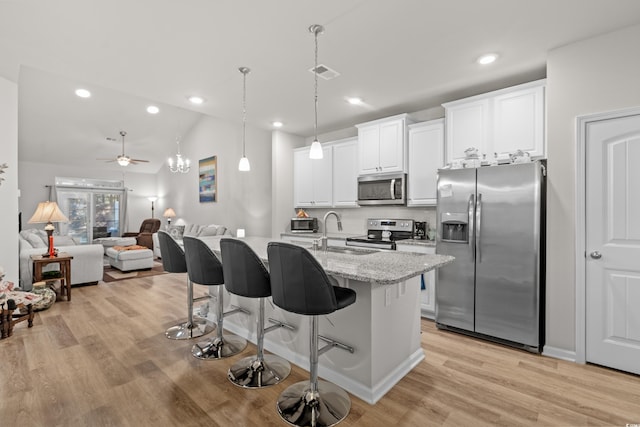 kitchen with a kitchen bar, sink, a center island with sink, stainless steel appliances, and light stone countertops