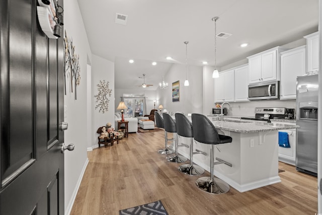 kitchen featuring light stone counters, white cabinetry, a center island with sink, and appliances with stainless steel finishes