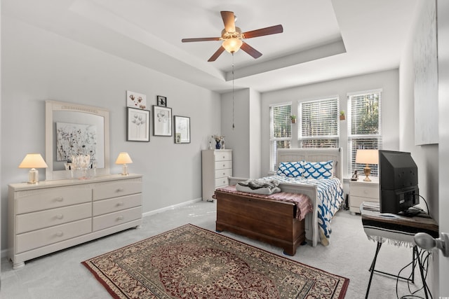 bedroom featuring ceiling fan, light colored carpet, and a tray ceiling