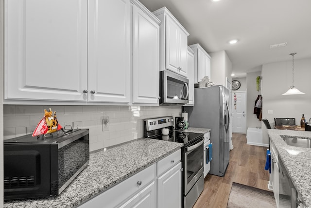 kitchen featuring appliances with stainless steel finishes, decorative light fixtures, white cabinets, light stone countertops, and light hardwood / wood-style flooring