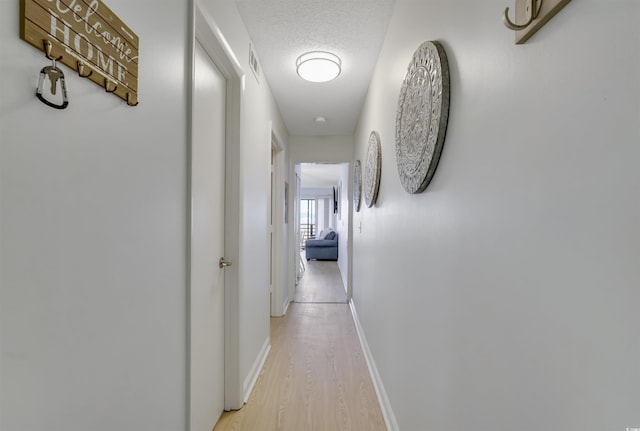 hallway featuring light hardwood / wood-style floors and a textured ceiling