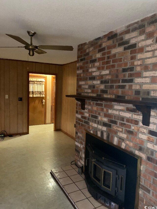 unfurnished living room featuring ceiling fan, wood walls, a textured ceiling, and a wood stove