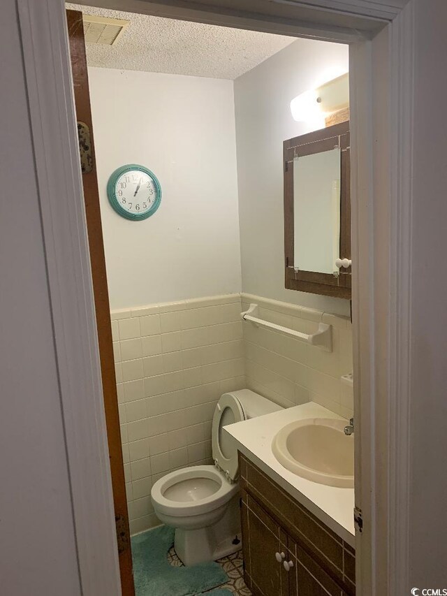 bathroom with tile walls, vanity, toilet, and a textured ceiling