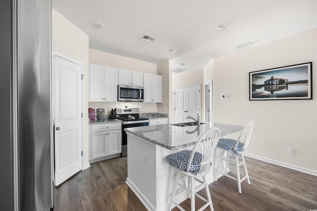 kitchen featuring white cabinets, a center island with sink, light stone counters, and stainless steel appliances