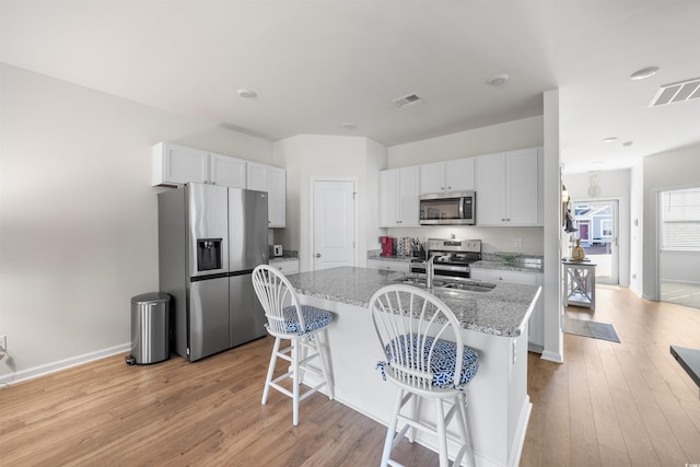 kitchen featuring an island with sink, light stone countertops, appliances with stainless steel finishes, and white cabinets