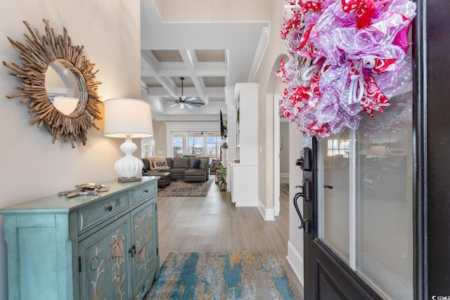 foyer entrance with ceiling fan, coffered ceiling, ornamental molding, beamed ceiling, and light wood-type flooring