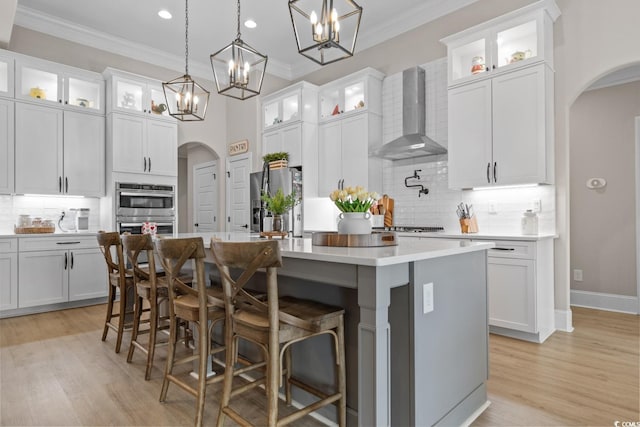 kitchen featuring a kitchen island with sink, white cabinets, and wall chimney exhaust hood