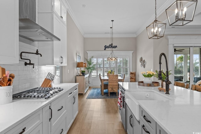 kitchen featuring white cabinets, decorative light fixtures, wall chimney exhaust hood, and appliances with stainless steel finishes