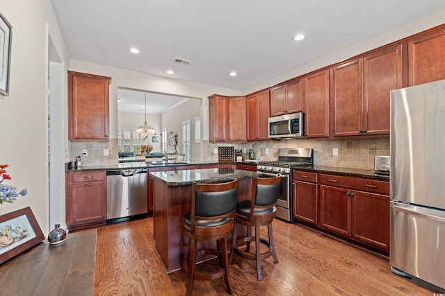 kitchen with sink, light hardwood / wood-style flooring, appliances with stainless steel finishes, kitchen peninsula, and dark stone counters