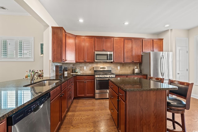 kitchen with sink, a breakfast bar, dark stone countertops, stainless steel appliances, and kitchen peninsula