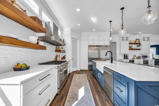 kitchen with pendant lighting, white cabinets, premium appliances, exhaust hood, and blue cabinetry