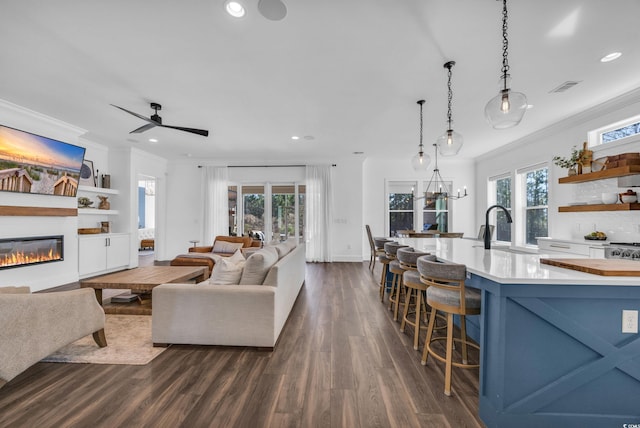 living room featuring dark hardwood / wood-style flooring, sink, ceiling fan with notable chandelier, and ornamental molding