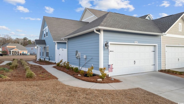 view of side of home featuring a garage, driveway, and a shingled roof