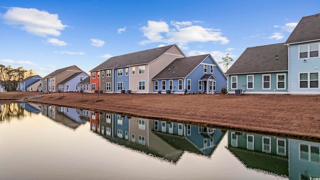 back of house featuring a residential view, a water view, a lawn, and central AC unit