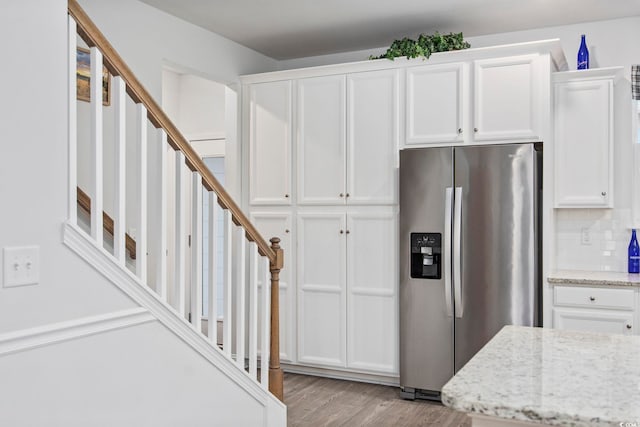 kitchen with light stone countertops, stainless steel fridge, backsplash, and white cabinetry