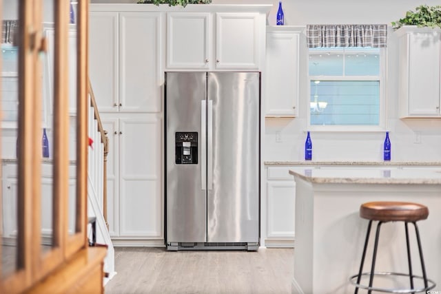 kitchen with light stone counters, stainless steel refrigerator with ice dispenser, tasteful backsplash, light wood-style floors, and white cabinets