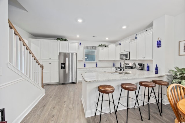 kitchen with appliances with stainless steel finishes, white cabinets, a sink, light stone countertops, and a peninsula