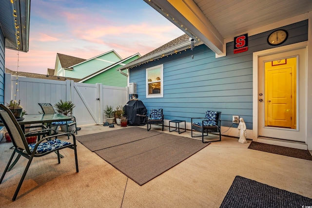 patio terrace at dusk with a gate, fence, and grilling area