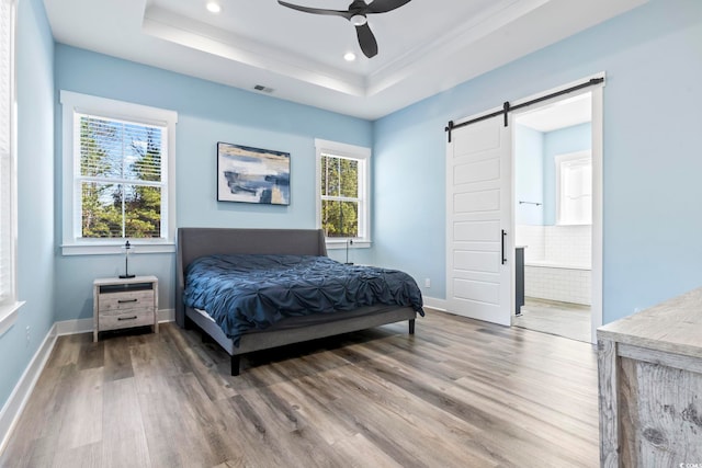 bedroom featuring ensuite bath, wood-type flooring, a barn door, and a raised ceiling