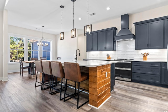 kitchen featuring premium range hood, a kitchen island with sink, a breakfast bar, and double oven range