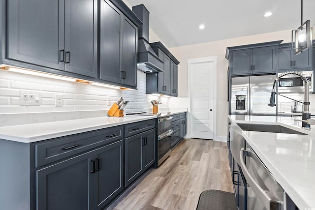 kitchen featuring premium range hood, decorative light fixtures, tasteful backsplash, stainless steel appliances, and light hardwood / wood-style flooring