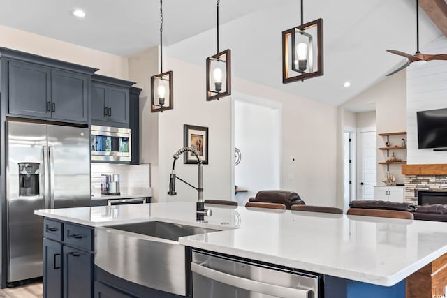 kitchen with pendant lighting, appliances with stainless steel finishes, light stone countertops, and a center island with sink