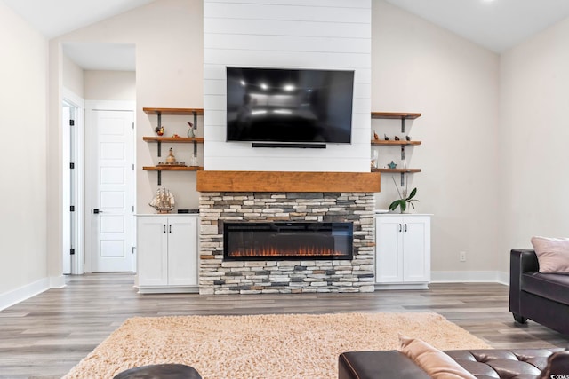 living room featuring hardwood / wood-style flooring, vaulted ceiling, and a stone fireplace