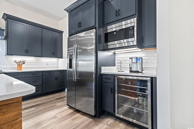 kitchen featuring tasteful backsplash, appliances with stainless steel finishes, beverage cooler, and light hardwood / wood-style flooring