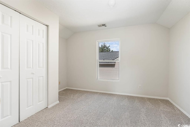 unfurnished bedroom featuring carpet flooring, vaulted ceiling, and a closet