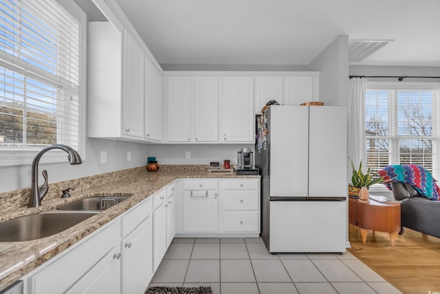 kitchen with light tile patterned flooring, white fridge, sink, white cabinetry, and a healthy amount of sunlight