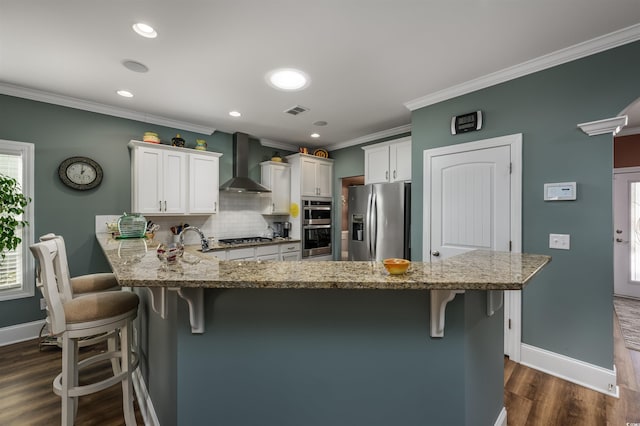 kitchen with wall chimney exhaust hood, white cabinetry, stainless steel appliances, and kitchen peninsula