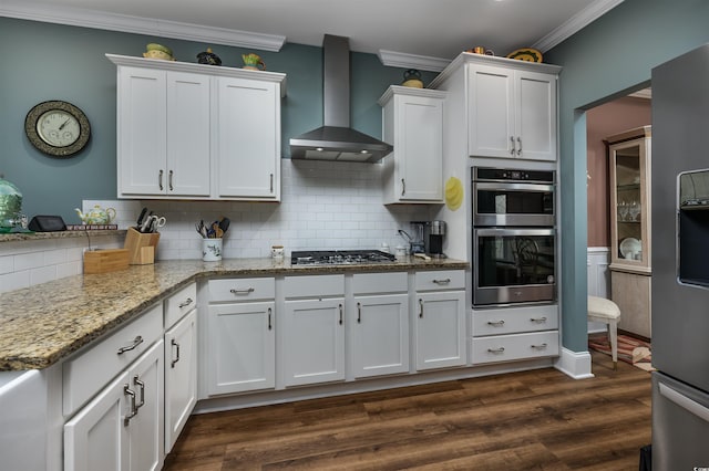 kitchen with wall chimney range hood, crown molding, stainless steel appliances, light stone countertops, and white cabinets