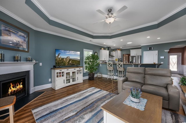 living room with a raised ceiling, crown molding, ceiling fan, and dark hardwood / wood-style flooring