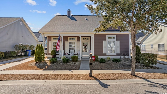 view of front of house featuring a porch, a chimney, a shingled roof, and fence