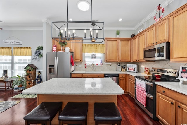 kitchen with a kitchen island, a breakfast bar area, ornamental molding, stainless steel appliances, and a sink