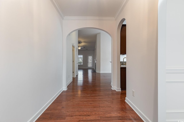 hallway featuring baseboards, dark wood finished floors, ornamental molding, arched walkways, and a sink