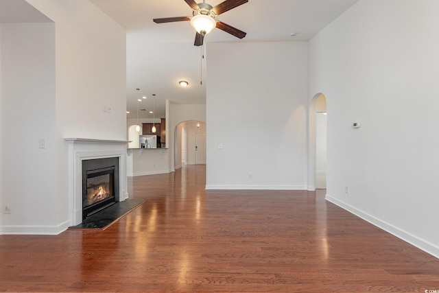 unfurnished living room featuring a glass covered fireplace, wood finished floors, arched walkways, and a ceiling fan