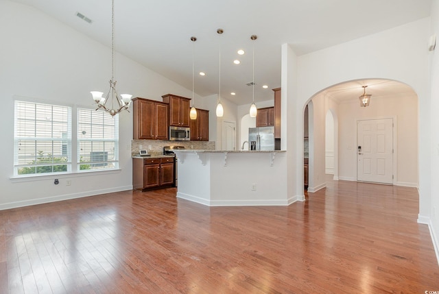 kitchen featuring visible vents, open floor plan, a breakfast bar, brown cabinetry, and stainless steel appliances