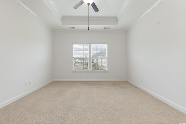 spare room with a tray ceiling, light colored carpet, visible vents, and ornamental molding