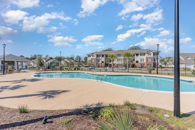 community pool with a patio, fence, and a residential view