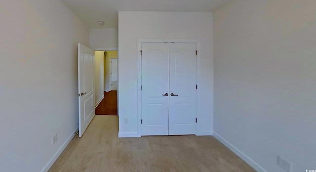 unfurnished bedroom with a closet, light carpet, and baseboards