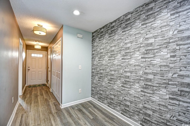 corridor featuring baseboards, wood finished floors, and a textured ceiling